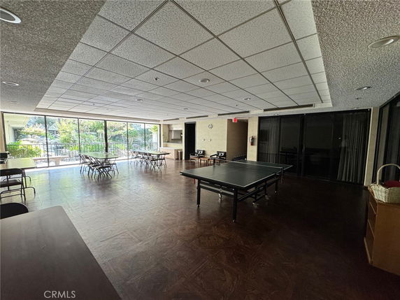 Indoor recreation area with large windows, chairs, tables, and a table tennis setup.