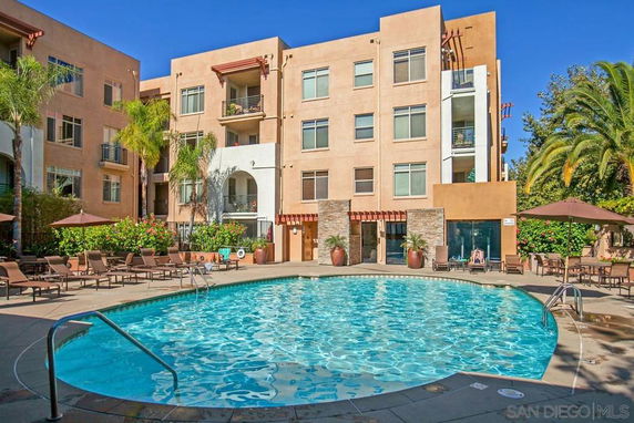 Outdoor swimming pool area in front of a multi-story residential building.