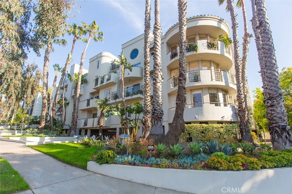 Front view of a modern multi-story building with balconies and a landscaped entrance.