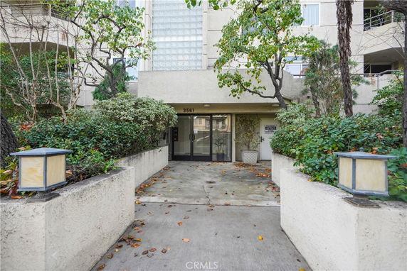Front view of a multi-story building entrance with trees and shrubs.
