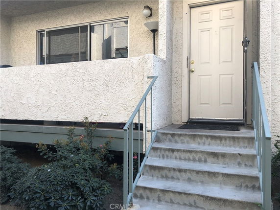 Front view of a building with a staircase leading to the entrance door and a small balcony.