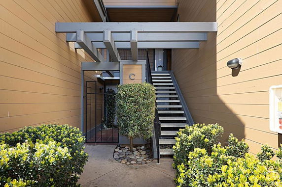 Front view of a stairway entrance in an outdoor building corridor with plants and wooden panels.
