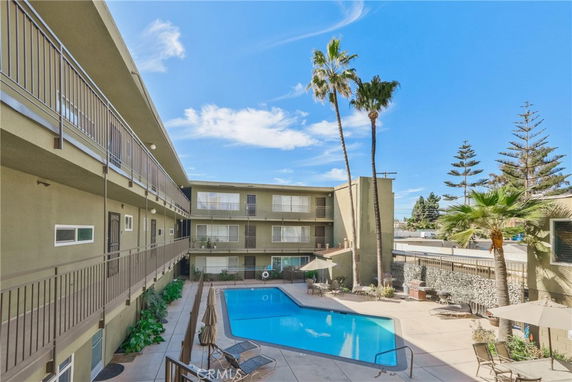 Outdoor area with a swimming pool surrounded by a multi-story residential building and palm trees.