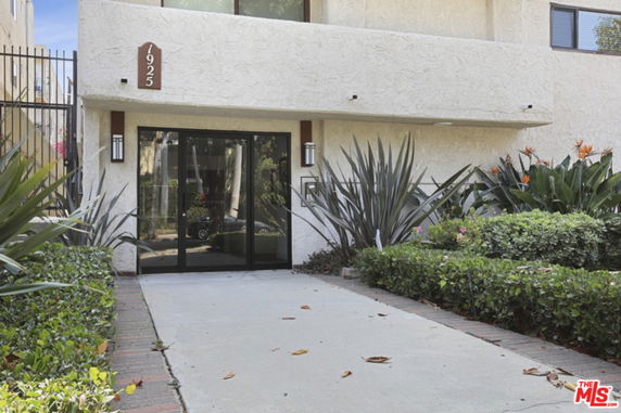Front entrance of a building with glass doors and surrounding plants.