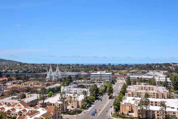 Panoramic view of a cityscape with buildings and a distant ocean horizon under a clear blue sky.