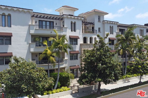Front view of a multi-story residential building with balconies and lush greenery.