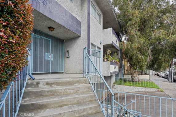 Entrance view of a multi-story building with stairs and blue railings.