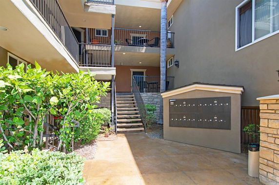 Front view of a multi-story apartment building with balconies and a mailbox area.