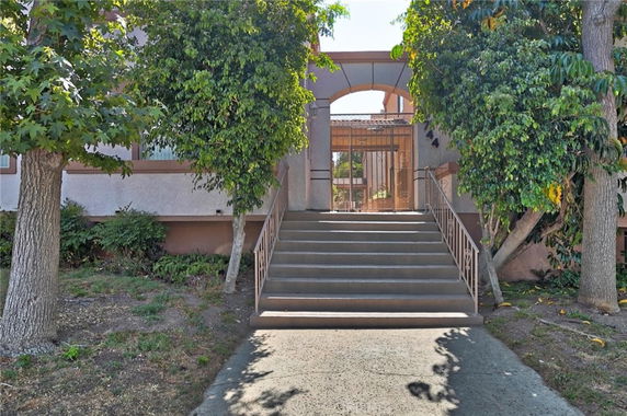 Front view of a building with stairs leading to a gated entrance.