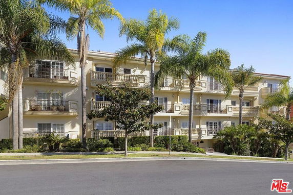 Front view of a multi-story apartment building with several balconies and palm trees in front.