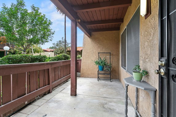 Covered outdoor patio area at the entrance of a house with potted plants and railing.