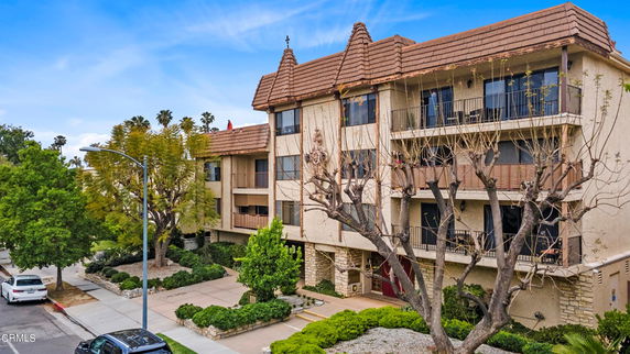 Front view of a multi-story apartment building with balconies and a sloped roof.