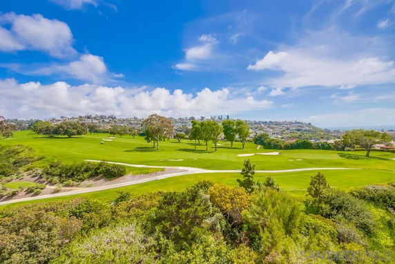 Panoramic view of a golf course with trees and a distant view of a town.