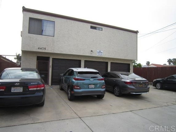 Parking area in front of a two-story building with multiple cars parked.