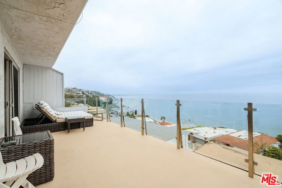 Outdoor balcony with lounge chairs and a glass railing overlooking the ocean.