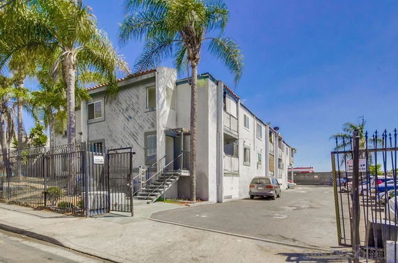 Front view of a multi-story residential building with a gated entrance and palm trees.
