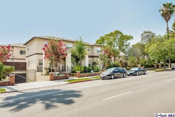 Front view of a two-story residential building with surrounding trees and parked cars.