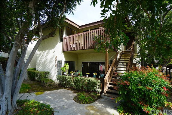 Front view of a two-story building with an outdoor staircase and a wooden balcony.