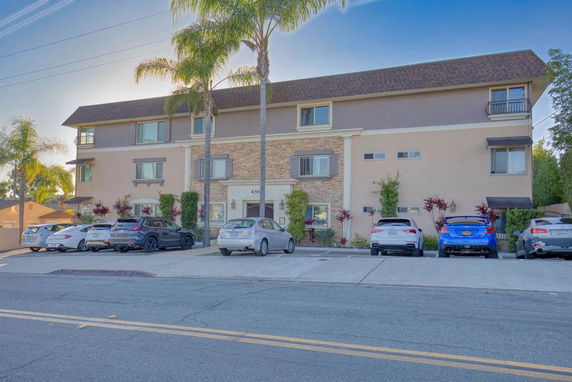 Front view of a three-story residential building with parked cars in front.