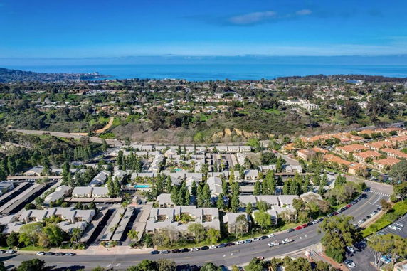 Aerial view of a residential area with houses, roads, and greenery, overlooking the coastline and ocean.