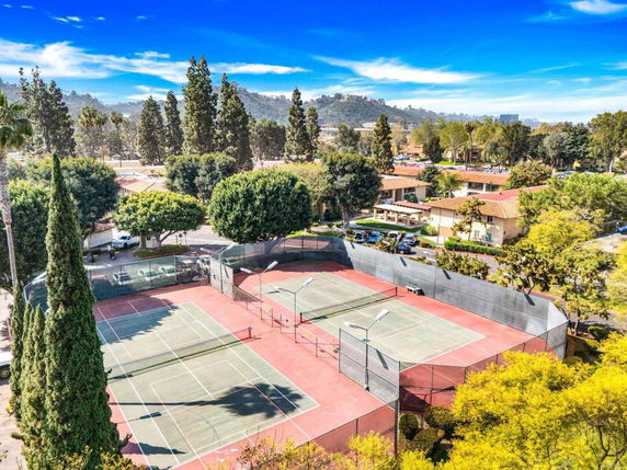 Aerial view of outdoor tennis courts with nearby residential buildings and trees.
