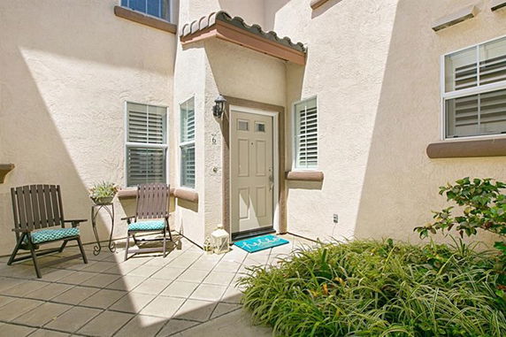 Front view of a house entrance with light-colored walls, a door with sidelights, and a small patio area.