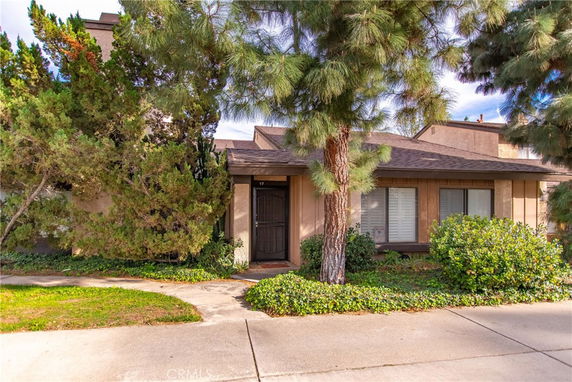 Front view of a single-story house with trees and shrubs in the foreground.