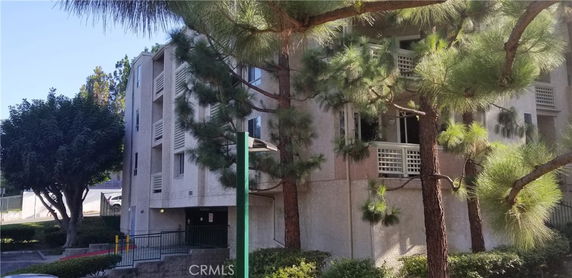 Front view of a multi-story residential building with balconies and surrounded by trees.