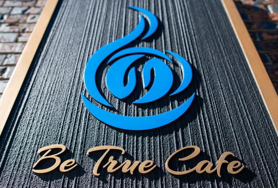 Close-up view of a cafe signage with a blue logo and 'Be True Cafe' text.