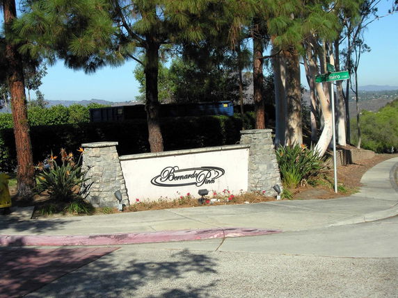 Entrance sign for a residential area with trees and a street corner.