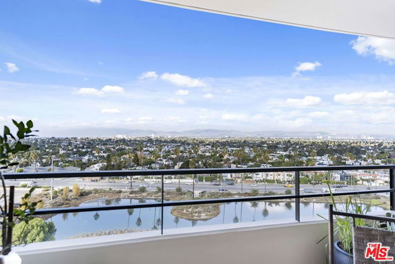 Wide angle view from a balcony overlooking a cityscape with buildings and distant mountains under a blue sky.