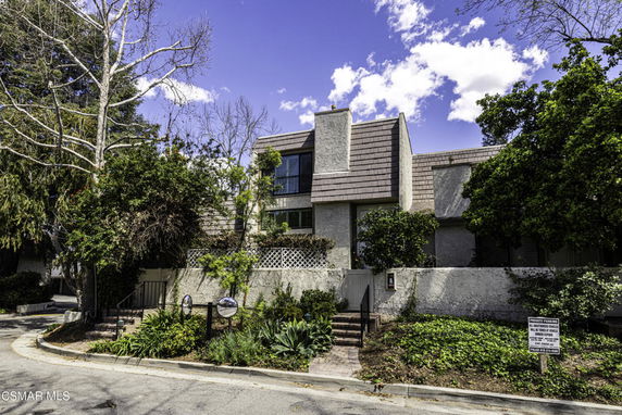 Front view of a two-story house with a unique sloped roof and chimney, surrounded by trees.