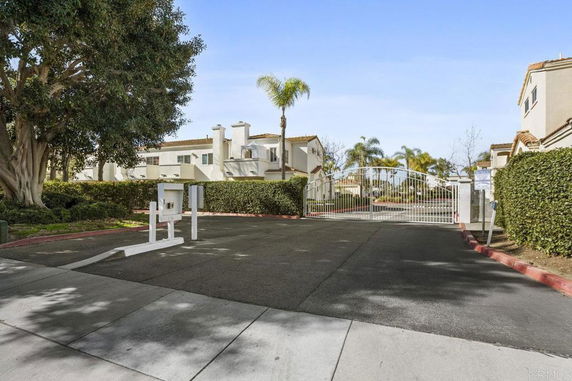 Front view of a gated community with white buildings and palm trees.