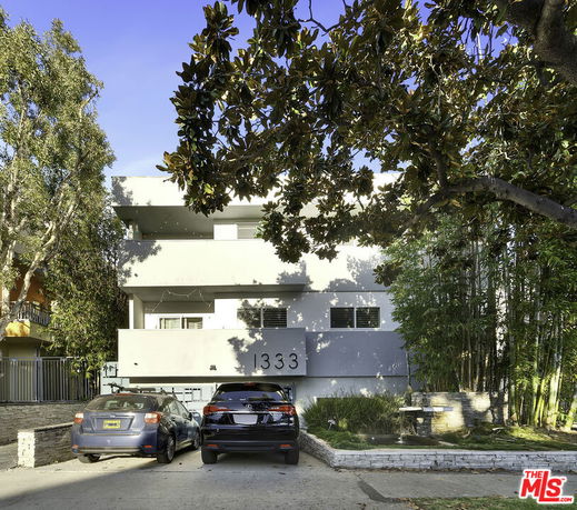 Front view of a multi-story building with a flat roof and two cars parked in the driveway.