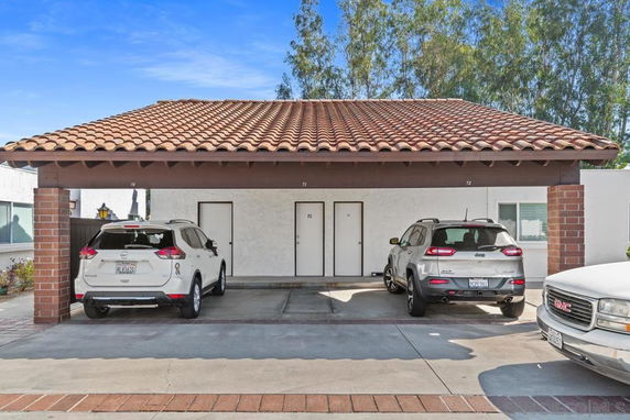 Covered parking area with three vehicles under a tiled roof structure.