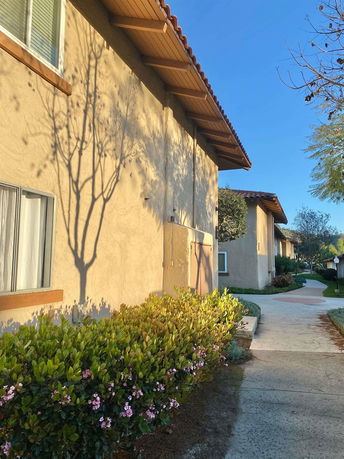 Side view of a building with stucco walls and a tiled roof, surrounded by a pathway and landscaping.