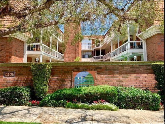 Front view of a brick multi-story building with balconies and a surrounding wall.