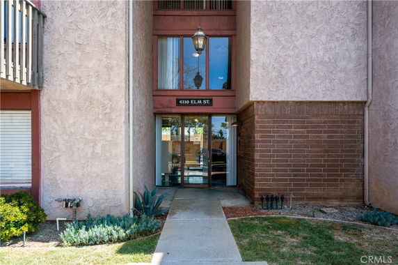 Front view of a multi-story building entrance with glass doors and a combination of stucco and brick exterior.