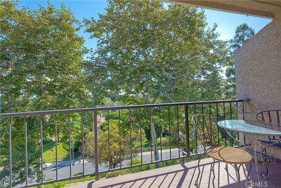 View from a balcony with railing, overlooking trees and a road.