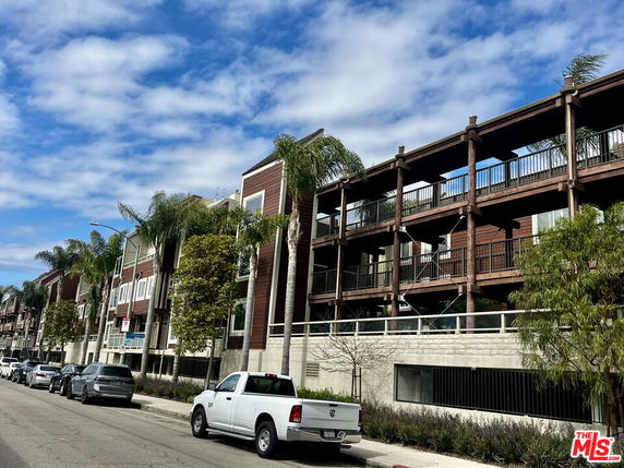 Side view of a multi-story building with balconies and palm trees.