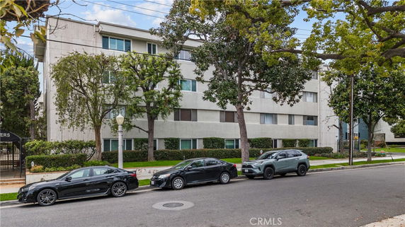 Front view of a multi-story apartment building with cars parked on the street.