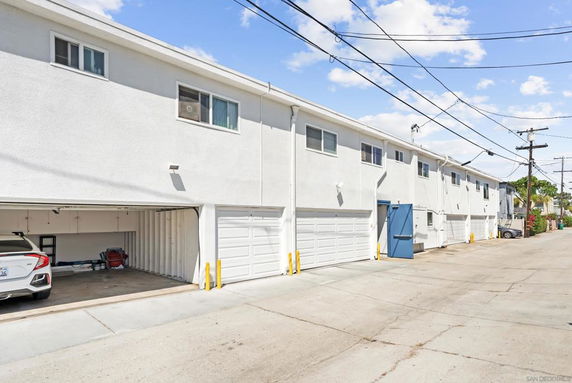 Outdoor view of a multi-unit building with garages and open parking spaces.