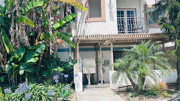 Front view of a multi-story house with a balcony and surrounding greenery.