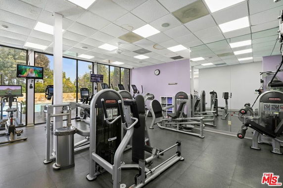 Indoor gym area with various exercise machines and large windows.