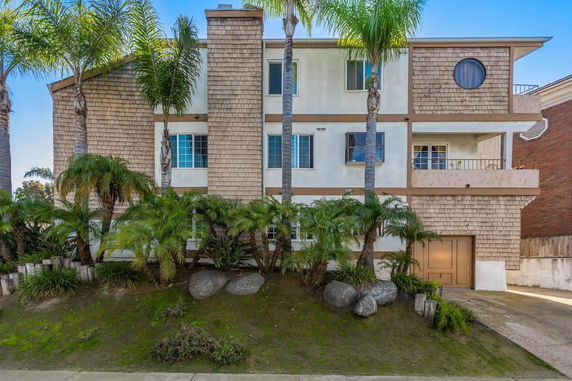 Front view of a multi-story house with shingle siding and surrounded by palm trees.