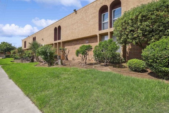 Front view of a rectangular two-story building with arched windows and surrounding greenery.
