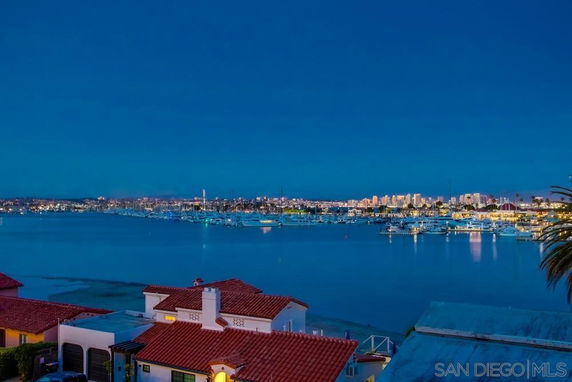 View of a calm bay with boats and a cityscape in the distance during twilight.