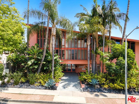 Front view of a pink multi-story building with large windows and surrounded by palm trees.