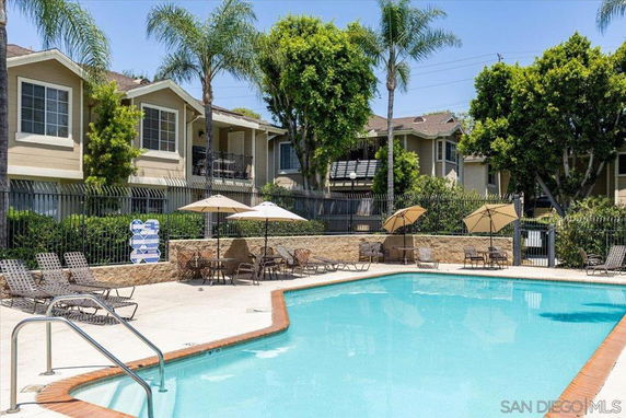 Outdoor swimming pool with surrounding patio and umbrellas in front of residential buildings.