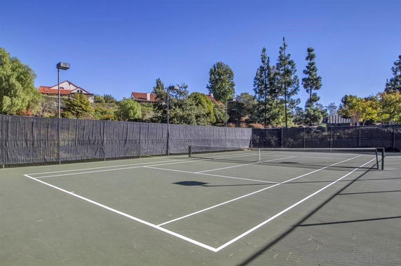 Outdoor tennis court surrounded by a fence and trees.